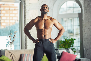 Image showing Young african-american man teaching at home online courses of fitness, aerobic, sporty lifestyle while being quarantine