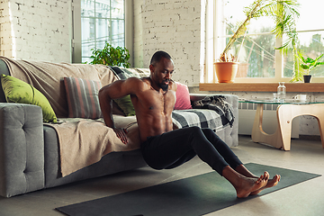 Image showing Young african-american man teaching at home online courses of fitness, aerobic, sporty lifestyle while being quarantine