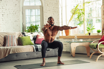 Image showing Young african-american man teaching at home online courses of fitness, aerobic, sporty lifestyle while being quarantine