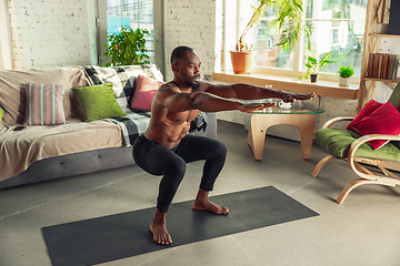 Image showing Young african-american man teaching at home online courses of fitness, aerobic, sporty lifestyle while being quarantine