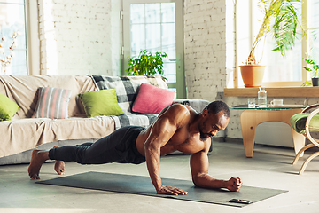 Image showing Young african-american man teaching at home online courses of fitness, aerobic, sporty lifestyle while being quarantine