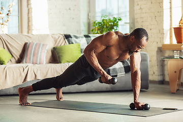 Image showing Young african-american man teaching at home online courses of fitness, aerobic, sporty lifestyle while being quarantine