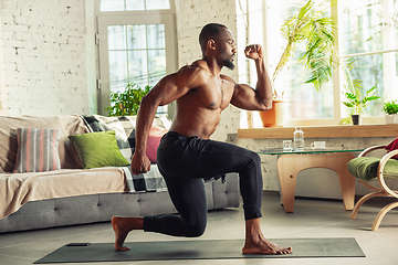 Image showing Young african-american man teaching at home online courses of fitness, aerobic, sporty lifestyle while being quarantine