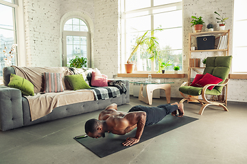 Image showing Young african-american man teaching at home online courses of fitness, aerobic, sporty lifestyle while being quarantine