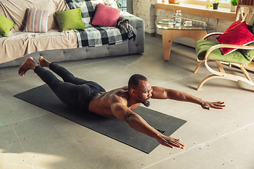 Image showing Young african-american man teaching at home online courses of fitness, aerobic, sporty lifestyle while being quarantine