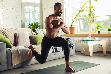 Image showing Young african-american man teaching at home online courses of fitness, aerobic, sporty lifestyle while being quarantine