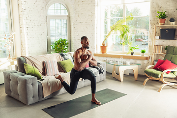 Image showing Young african-american man teaching at home online courses of fitness, aerobic, sporty lifestyle while being quarantine