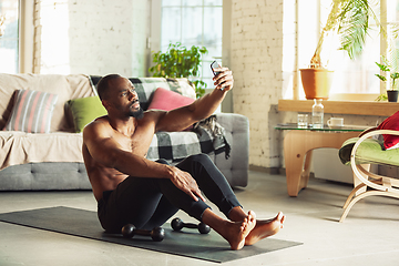 Image showing Young african-american man teaching at home online courses of fitness, aerobic, sporty lifestyle while being quarantine