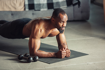 Image showing Young african-american man teaching at home online courses of fitness, aerobic, sporty lifestyle while being quarantine