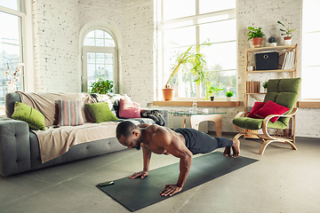 Image showing Young african-american man teaching at home online courses of fitness, aerobic, sporty lifestyle while being quarantine