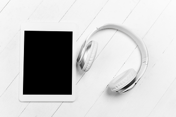 Image showing Tablet and headphones. Monochrome stylish composition in white color. Top view, flat lay.