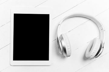 Image showing Tablet and headphones. Monochrome stylish composition in white color. Top view, flat lay.