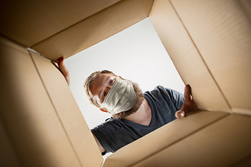 Image showing Young man opening the huge postal package wearing protective face mask, contactless delivery