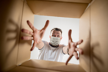 Image showing Young man opening the huge postal package wearing protective face mask, contactless delivery