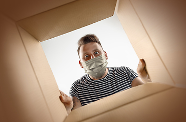 Image showing Young man opening the huge postal package wearing protective face mask, contactless delivery