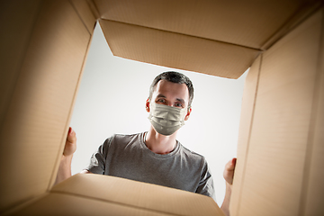 Image showing Young man opening the huge postal package wearing protective face mask, contactless delivery