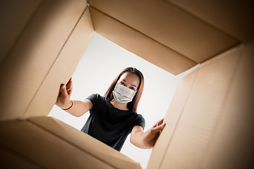 Image showing Young woman opening the huge postal package wearing protective face mask, contactless delivery