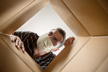 Image showing Young man opening the huge postal package wearing protective face mask, contactless delivery