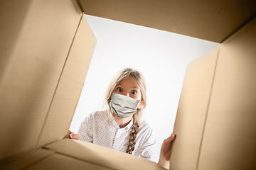 Image showing Little girl opening the huge postal package wearing protective face mask, contactless delivery