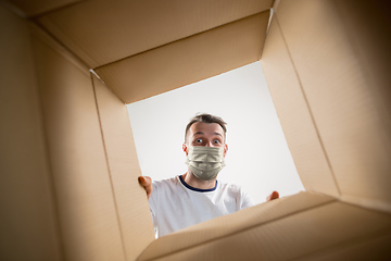 Image showing Young man opening the huge postal package wearing protective face mask, contactless delivery