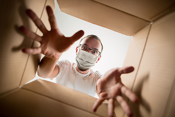 Image showing Young man opening the huge postal package wearing protective face mask, contactless delivery