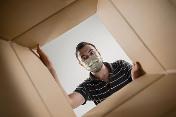 Image showing Young man opening the huge postal package wearing protective face mask, contactless delivery