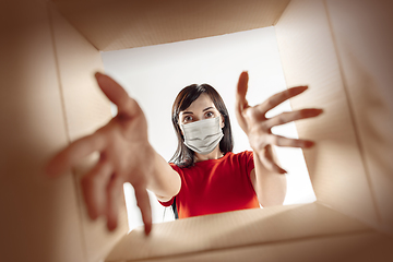 Image showing Young woman opening the huge postal package wearing protective face mask, contactless delivery