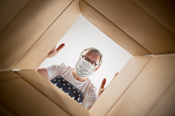 Image showing Senior man opening the huge postal package wearing protective face mask, contactless delivery