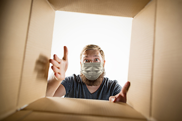 Image showing Young man opening the huge postal package wearing protective face mask, contactless delivery