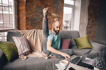 Image showing Young man doing yoga at home while being quarantine and freelance working