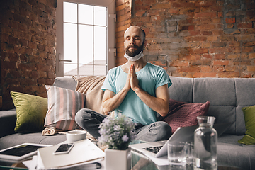 Image showing Young man doing yoga at home while being quarantine and freelance working