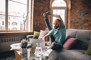 Image showing Young man doing yoga at home while being quarantine and freelance working