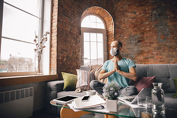 Image showing Young man doing yoga at home while being quarantine and freelance working