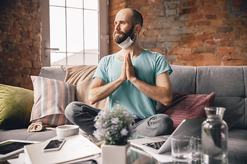 Image showing Young man doing yoga at home while being quarantine and freelance working