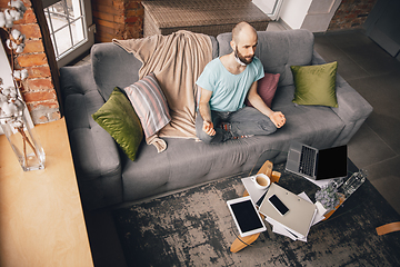 Image showing Young man doing yoga at home while being quarantine and freelance working