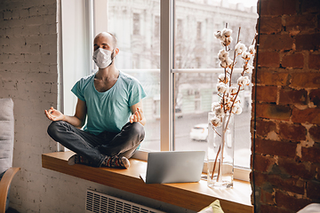 Image showing Young man doing yoga at home while being quarantine and freelance working