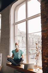 Image showing Young man doing yoga at home while being quarantine and freelance working