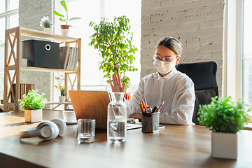 Image showing Woman working in office alone during coronavirus or COVID-19 quarantine, wearing face mask