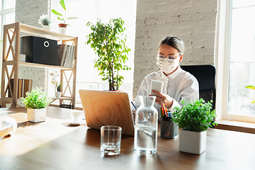 Image showing Woman working in office alone during coronavirus or COVID-19 quarantine, wearing face mask