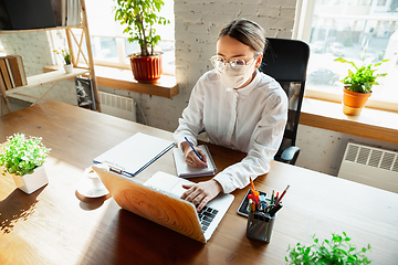 Image showing Woman working in office alone during coronavirus or COVID-19 quarantine, wearing face mask