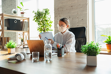 Image showing Woman working in office alone during coronavirus or COVID-19 quarantine, wearing face mask