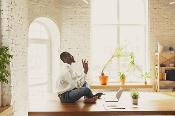 Image showing Young african-american man doing yoga at home while being quarantine and freelance working