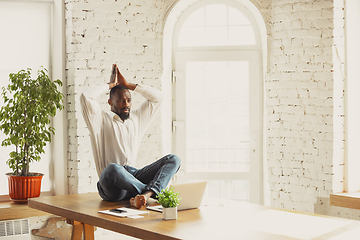 Image showing Young african-american man doing yoga at home while being quarantine and freelance working