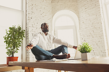 Image showing Young african-american man doing yoga at home while being quarantine and freelance working