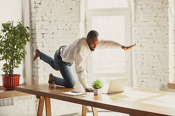 Image showing Young african-american man doing yoga at home while being quarantine and freelance working