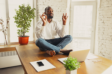 Image showing Young african-american man doing yoga at home while being quarantine and freelance working