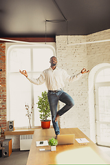 Image showing Young african-american man doing yoga at home while being quarantine and freelance working