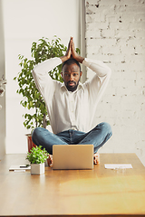 Image showing Young african-american man doing yoga at home while being quarantine and freelance working