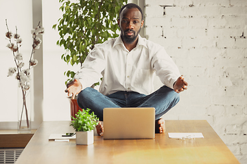 Image showing Young african-american man doing yoga at home while being quarantine and freelance working