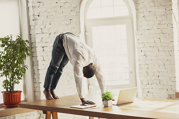 Image showing Young african-american man doing yoga at home while being quarantine and freelance working